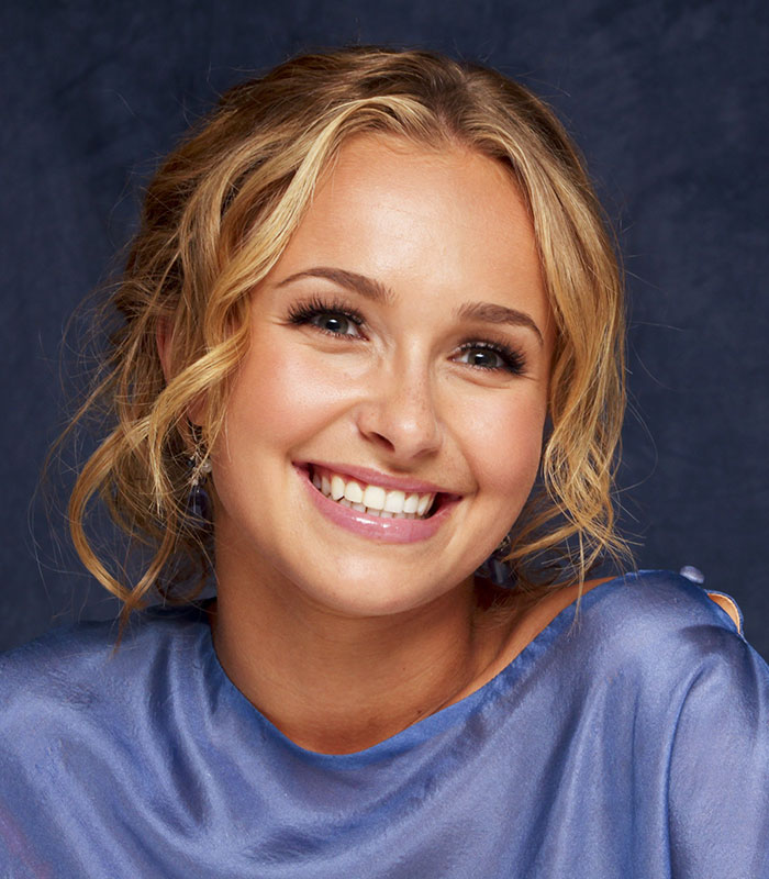 Young Hayden Panettiere smiling brightly, with curly blonde hair and wearing a blue top, against a dark blue background. Young Hayden Panettiere smiling brightly, with curly blonde hair and wearing a blue top, against a dark blue background.