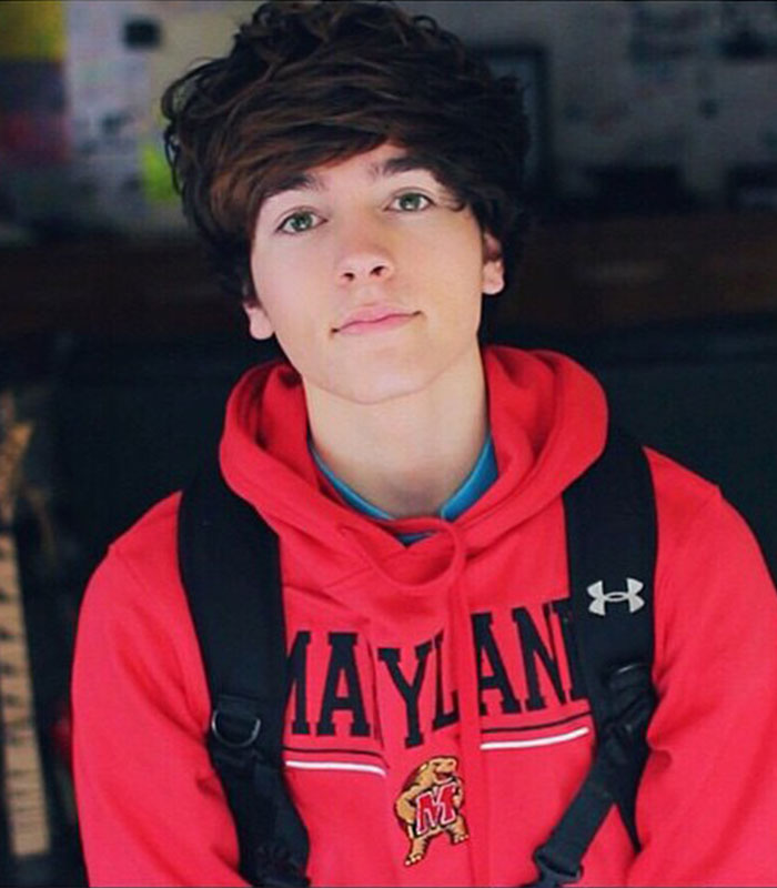 Young male influencer with dark curly hair wearing a red Maryland hoodie, among 11 influencers exposed for lying