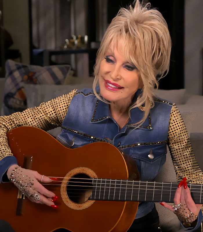 Dolly Parton playing guitar, showcasing her gloved hands with intricate designs. Dolly Parton playing guitar, showcasing her gloved hands with intricate designs.