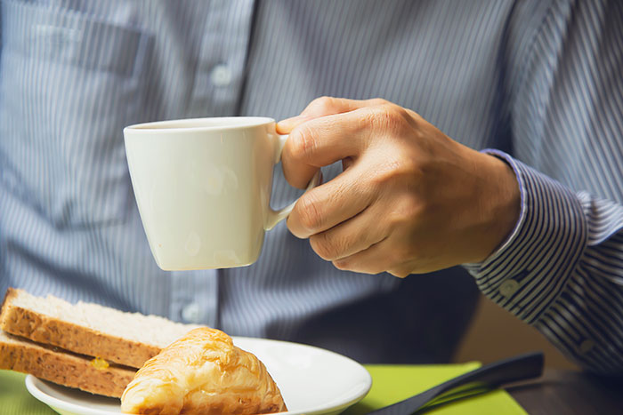 Man holding a coffee cup, with a croissant and toast for his breakfast habit, potentially increasing mortality risk after age 40. Man holding a coffee cup, with a croissant and toast for his breakfast habit, potentially increasing mortality risk after age 40.
