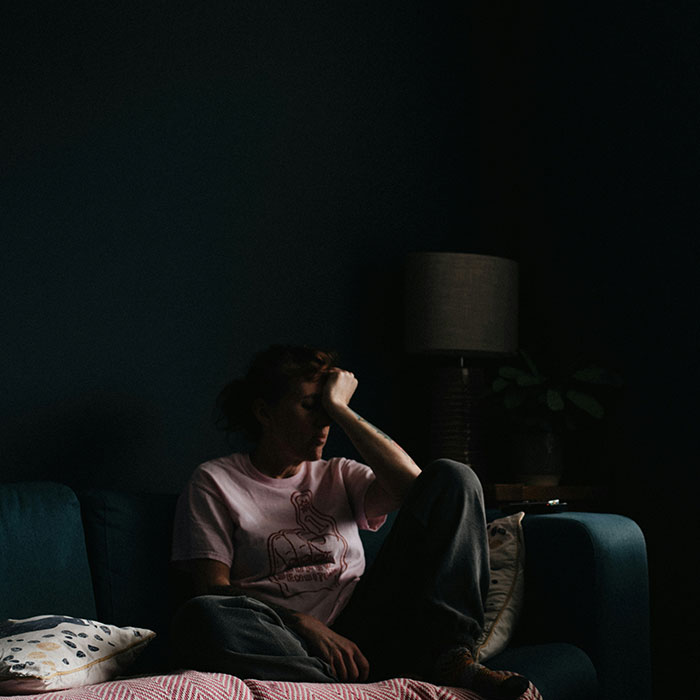 Woman sitting alone in a dark room, head in hand, depicting a cancer symptom of emotional distress. Woman sitting alone in a dark room, head in hand, depicting a cancer symptom of emotional distress.