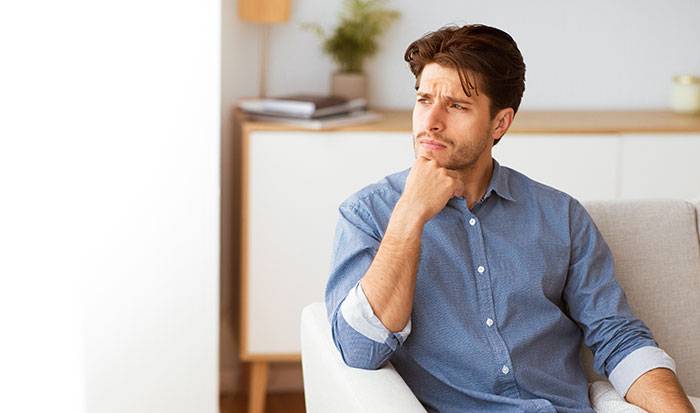 A man looking pensive and concerned, reflecting on his wife's jealousy, a secret police call, and the resulting deportation.