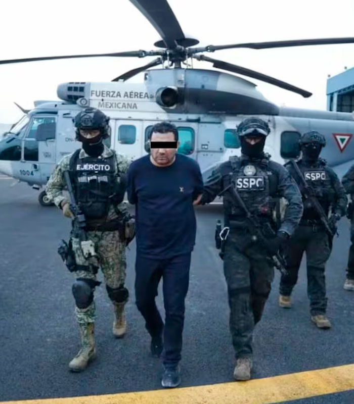 A cartel boss being escorted by armed officers in front of a Mexican Air Force helicopter. A cartel boss being escorted by armed officers in front of a Mexican Air Force helicopter.