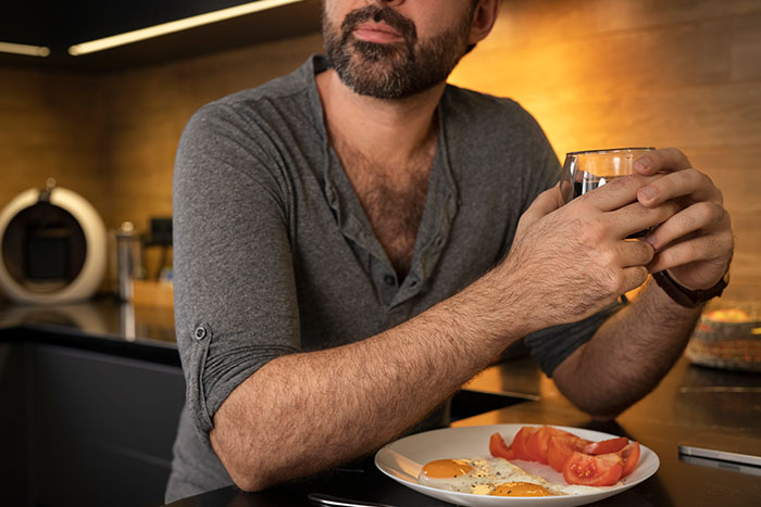 Man with a beard holding a drink, with eggs and tomatoes, illustrating a breakfast habit and mortality risk after 40. Man with a beard holding a drink, with eggs and tomatoes, illustrating a breakfast habit and mortality risk after 40.