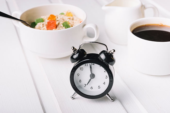 Alarm clock set for 7 AM, with oatmeal and coffee, representing a breakfast habit and mortality risk study. Alarm clock set for 7 AM, with oatmeal and coffee, representing a breakfast habit and mortality risk study.