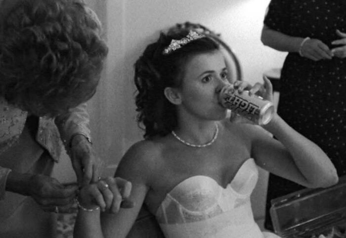 A bride sips from a can while another woman adjusts her wrist, an iconic funny wedding photo.