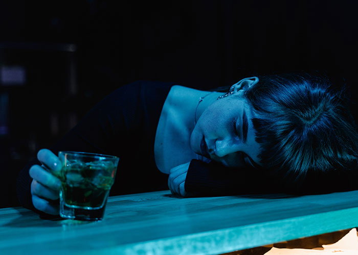 Woman in a dark bar, head down on the counter with a drink, depicting a terrible first date.