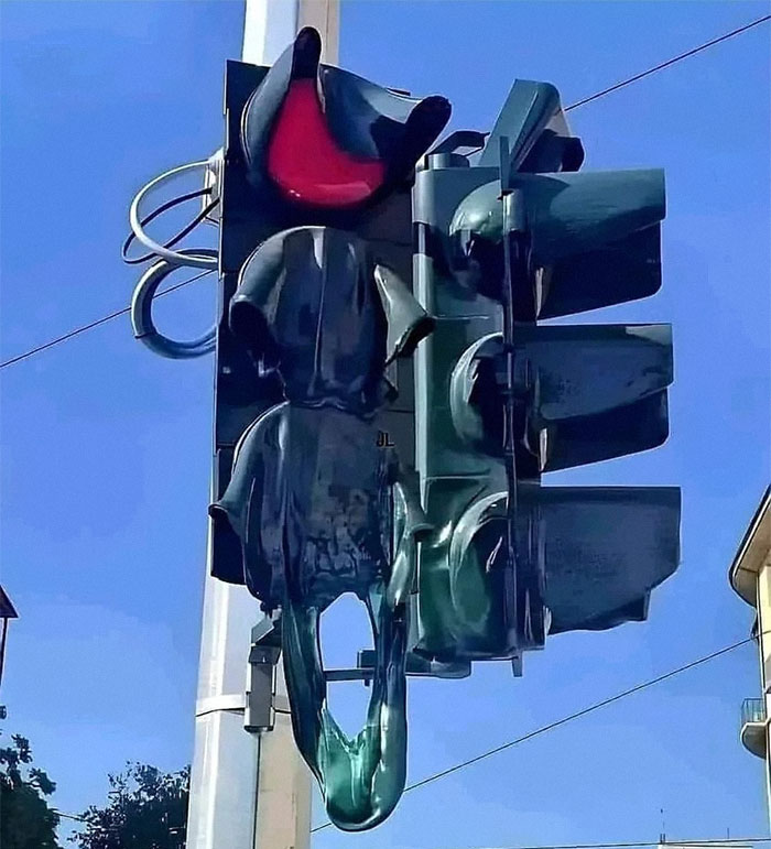 A traffic light with a red light on top, shows the effects of summer heat, with the entire structure appearing to be melting and dripping.