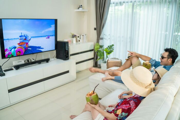 A couple in straw hats relaxes on a couch, enjoying a drink and watching TV, portraying truths about being married.