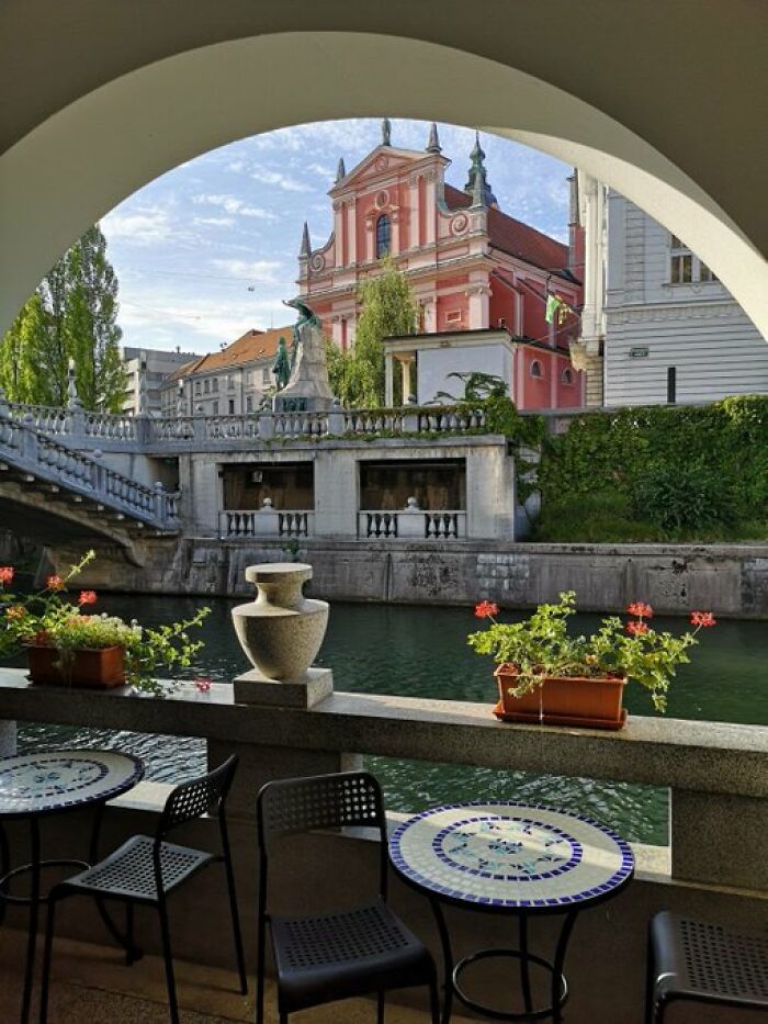 Charming cafe beside a river, offering views of a distinctive pink church, adding to the character of the buildings.