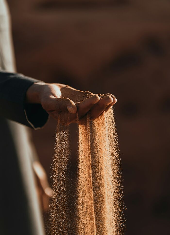 Sand sifting through fingers, representing cool scientific facts about geology and time.