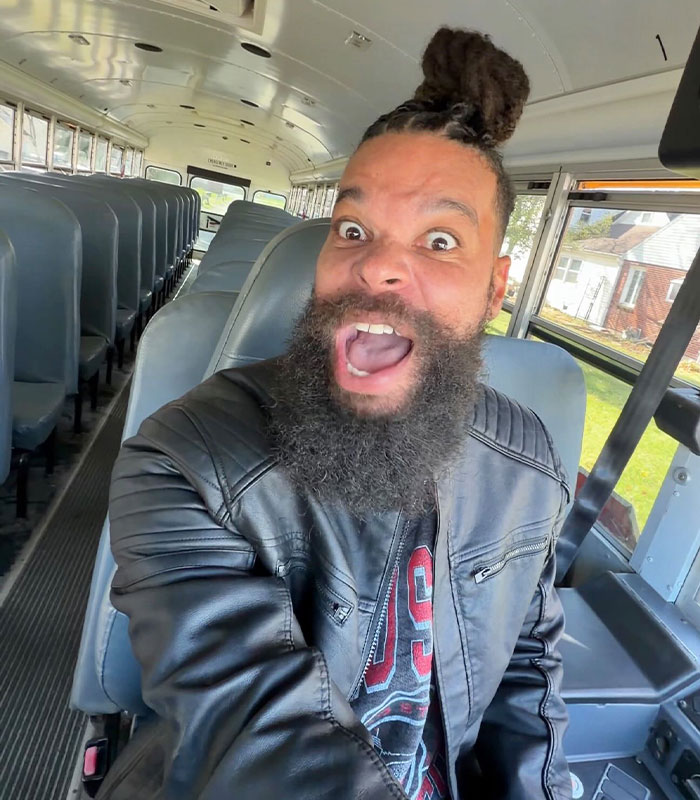 Influencer with a beard making a funny face while sitting in an empty school bus, expressing shock at a Walmart ban.