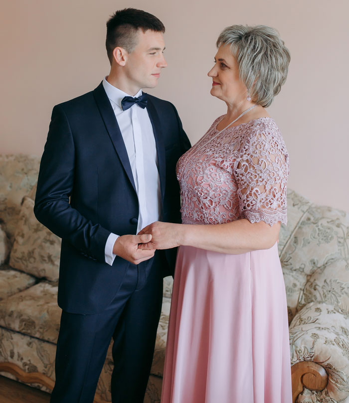 A young man in a suit holding an older woman's hand, possibly discussing shameful things that happened at weddings.