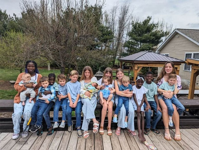 A large diverse family of children sitting on a porch, highlighting a couple adopting kids. A large diverse family of children sitting on a porch, highlighting a couple adopting kids.