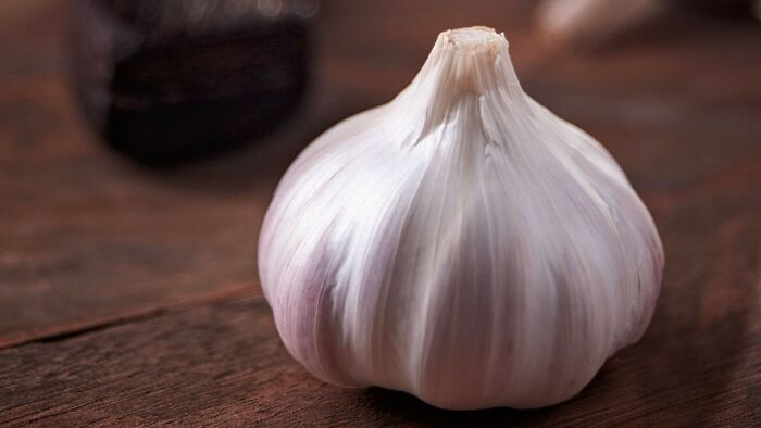 A close-up of a white garlic bulb on a wooden surface, relevant to controlling what a boyfriend eats.