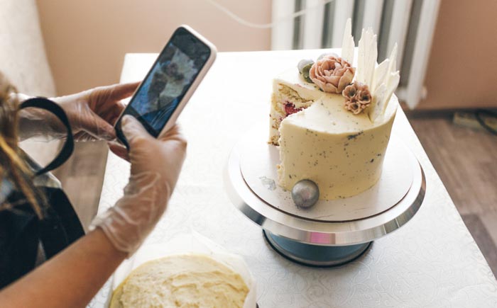A person in gloves taking a photo of a sliced cake on a stand, showcasing dumb work rules.