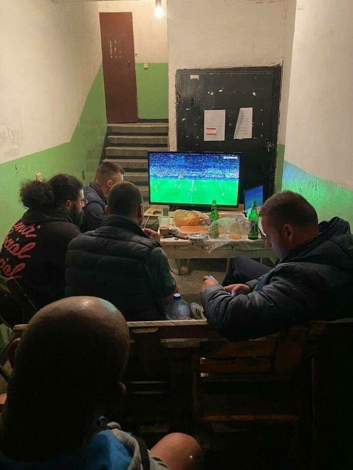 Men watching a football game on TV in a dimly lit room, showcasing how people from Eastern Europe are built different.