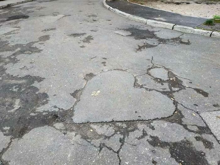 Eastern Europe meme: A heart-shaped pothole on a cracked asphalt road, showing unique characteristics.