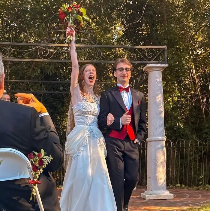 An iconic funny wedding photo of a bride raising her bouquet in triumph with her groom by her side after the ceremony.