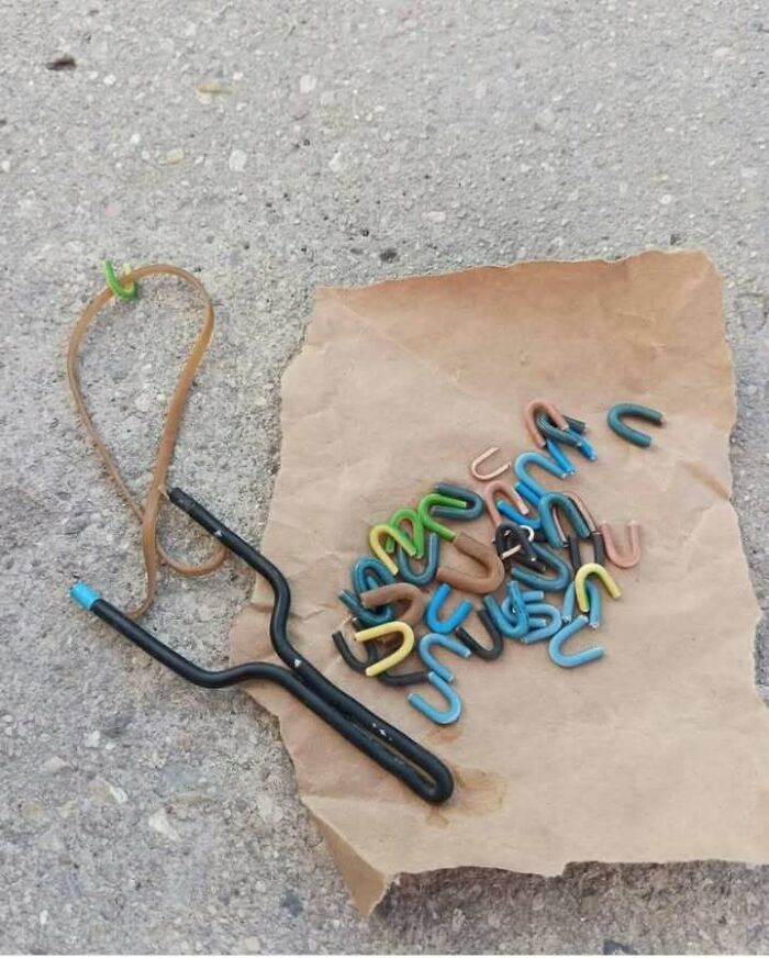 Slingshot with a pile of colorful u-shaped hooks on a brown paper bag, showcasing Eastern European resourcefulness.