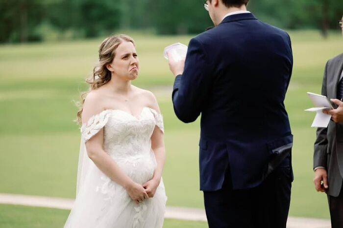 A funny wedding photo of a bride making a face while the groom reads his vows outdoors, showcasing an iconic moment.