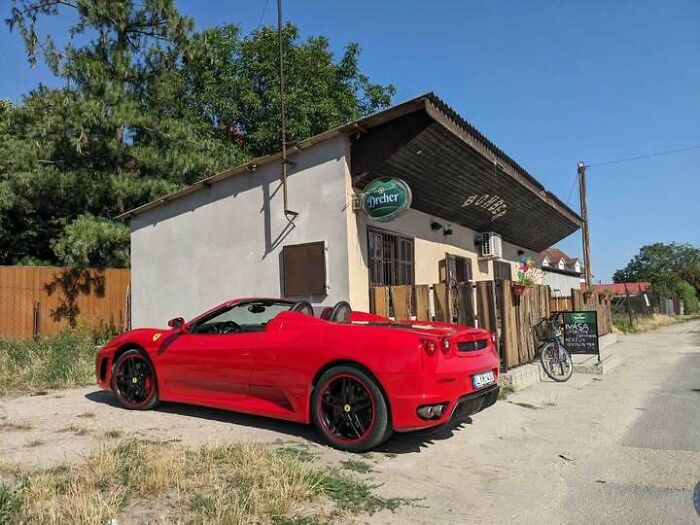 A red Ferrari convertible parked outside a simple building, highlighting that people from Eastern Europe are built different.