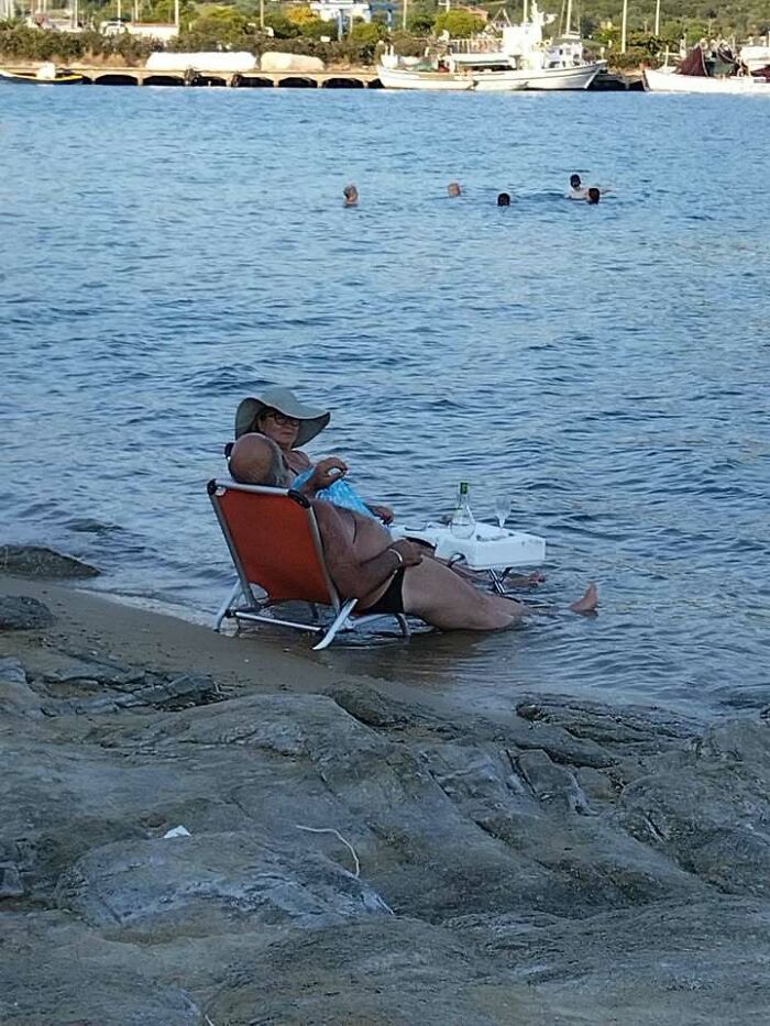 An elderly couple from Eastern Europe relaxing in beach chairs partly submerged in the water, showcasing a unique way to cool off.