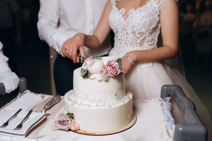 A newlywed couple cutting a two-tier wedding cake decorated with flowers. This image relates to dumb reasons couples divorce.