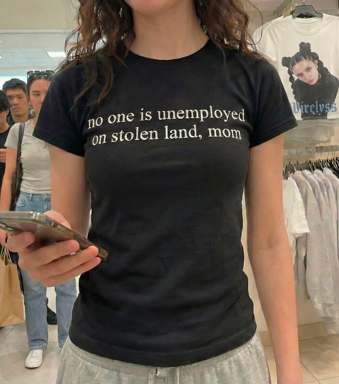 A person wears an iconic shirt saying: 'No one is unemployed on stolen land, mom.' in public.