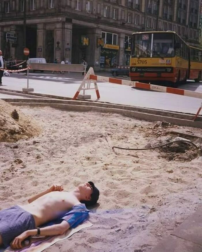 A meme of a man relaxing on sand by a road, showcasing why people from Eastern Europe are built different.