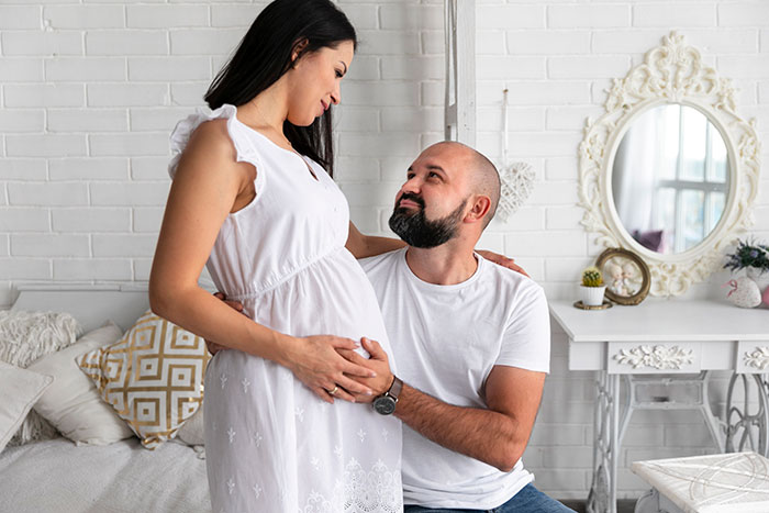 A couple, where spouses are sleeping together. Man looking up at a pregnant woman touching her belly. A couple, where spouses are sleeping together. Man looking up at a pregnant woman touching her belly.