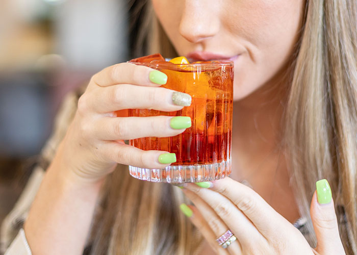 A woman sips a red cocktail, reflecting on worst first dates with women.