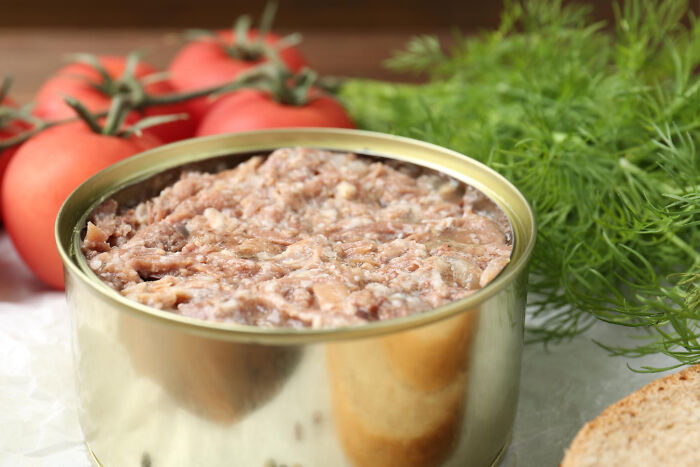An open can of meat next to tomatoes and dill, representing certain poverty habits.
