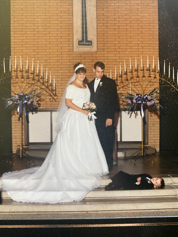 A young ring bearer lays on the steps below a standing bride and groom, an iconic funny wedding photo.