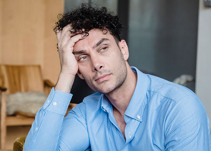 A man with a troubled expression, holding his head, reflecting on his worst first dates.