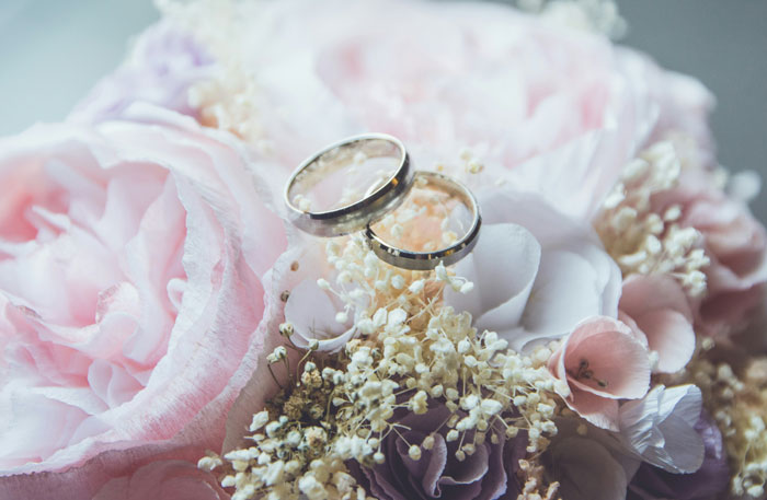 Two silver wedding rings nestled on a soft pink and white floral bouquet, symbolizing love at weddings.