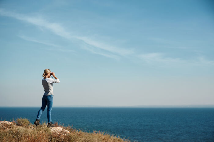 A woman looks through binoculars at the sea. People have many different healthy habits they believe in.