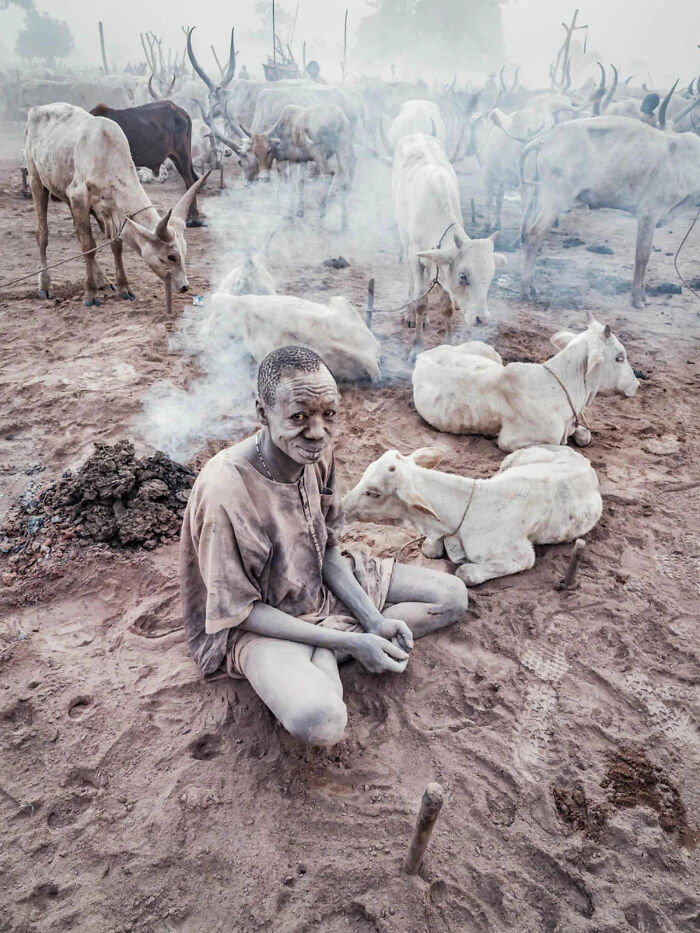A young boy with a dirt-covered face crouches on the ground, creating shapes from mud. This image won a 2026 European Photography Award.