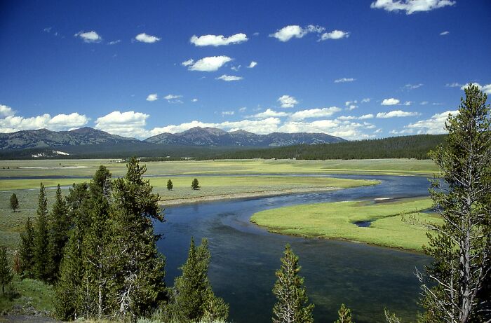 Vast landscape with a winding river, green fields, and distant mountains under a blue sky, showcasing scary science facts.