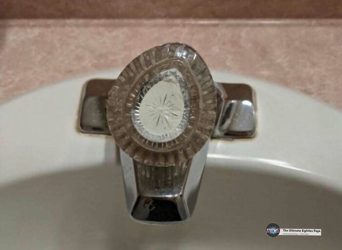 A close-up of a vintage 80s faucet handle with a clear, ridged design over a white sink, reminding you of the good time you had.
