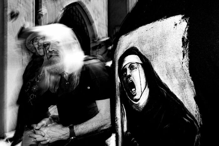 A blurry image of a man with long hair next to a dark painting of a screaming nun, a dramatic street photography award entry.