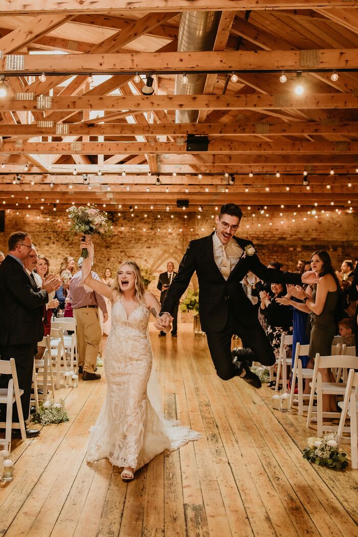 A bride and groom celebrating, the groom captured mid-air jump in a Funny Wedding Photos reception entrance.