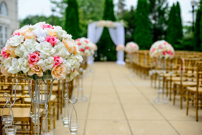 An aisle decorated with floral arrangements and gold chairs for an outdoor wedding ceremony, depicting wedding setup.