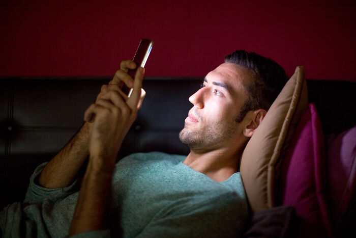 A man in bed looking at his phone, illustrating a healthy habit that might be glorified but isn't always good.