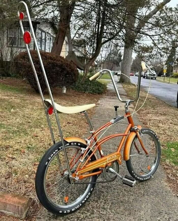 An orange and white vintage bicycle with high handlebars and a banana seat, reminiscent of the 80s good time.