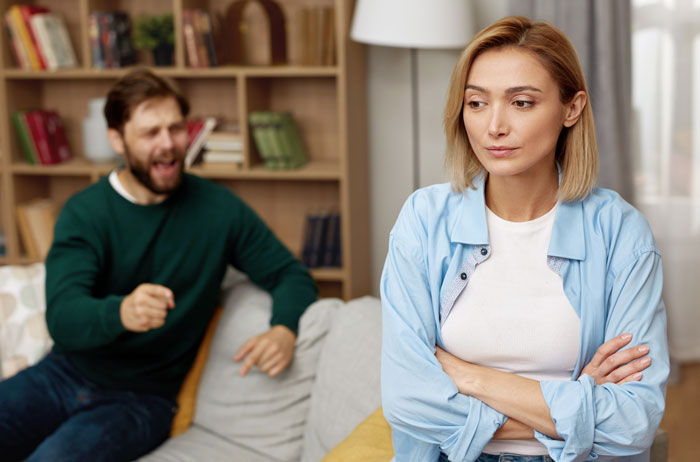 A woman looks frustrated as her husband yells, showing the strain of his mom controlling their marriage. A woman looks frustrated as her husband yells, showing the strain of his mom controlling their marriage.