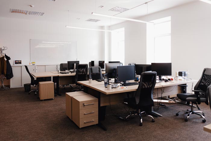 An empty office with several desks and computer monitors, reflecting dumb work rules.
