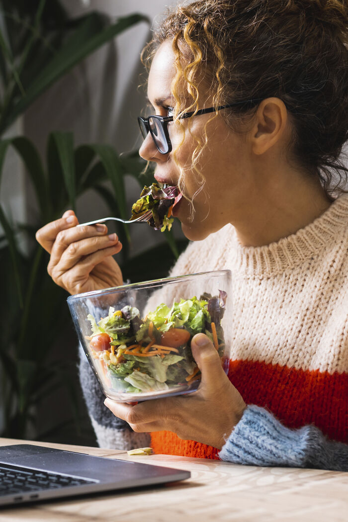 A woman eats a healthy salad while looking at a laptop. Eating healthy foods is one of the important healthy habits.
