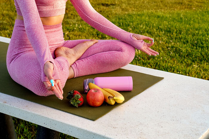 A woman in pink yoga attire meditating outdoors with healthy fruit and water bottle, a wellness practice doctors refuse to compromise.