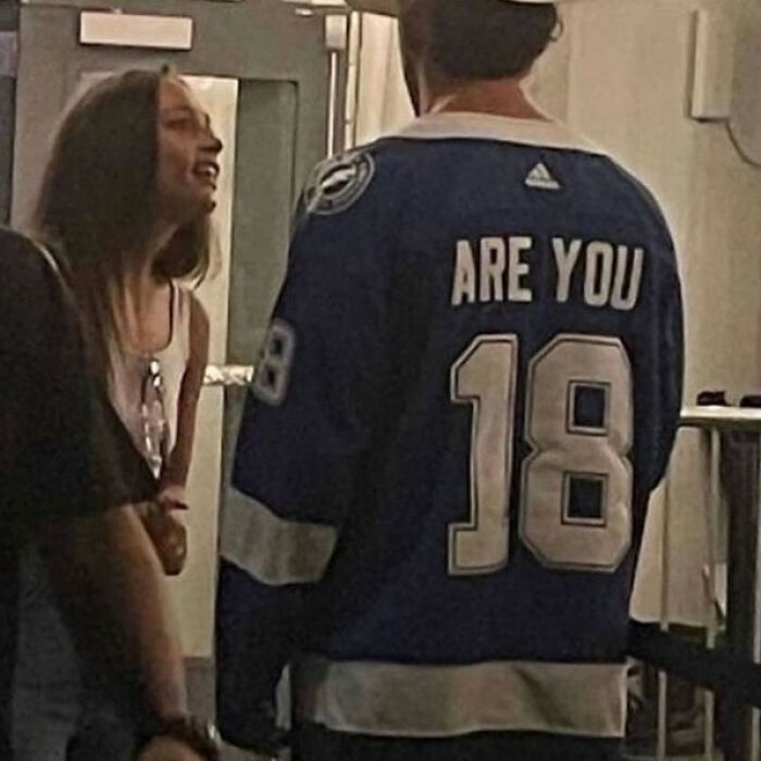 A man wearing an iconic hockey jersey with the number 18 and Are You above it, talking to a woman.